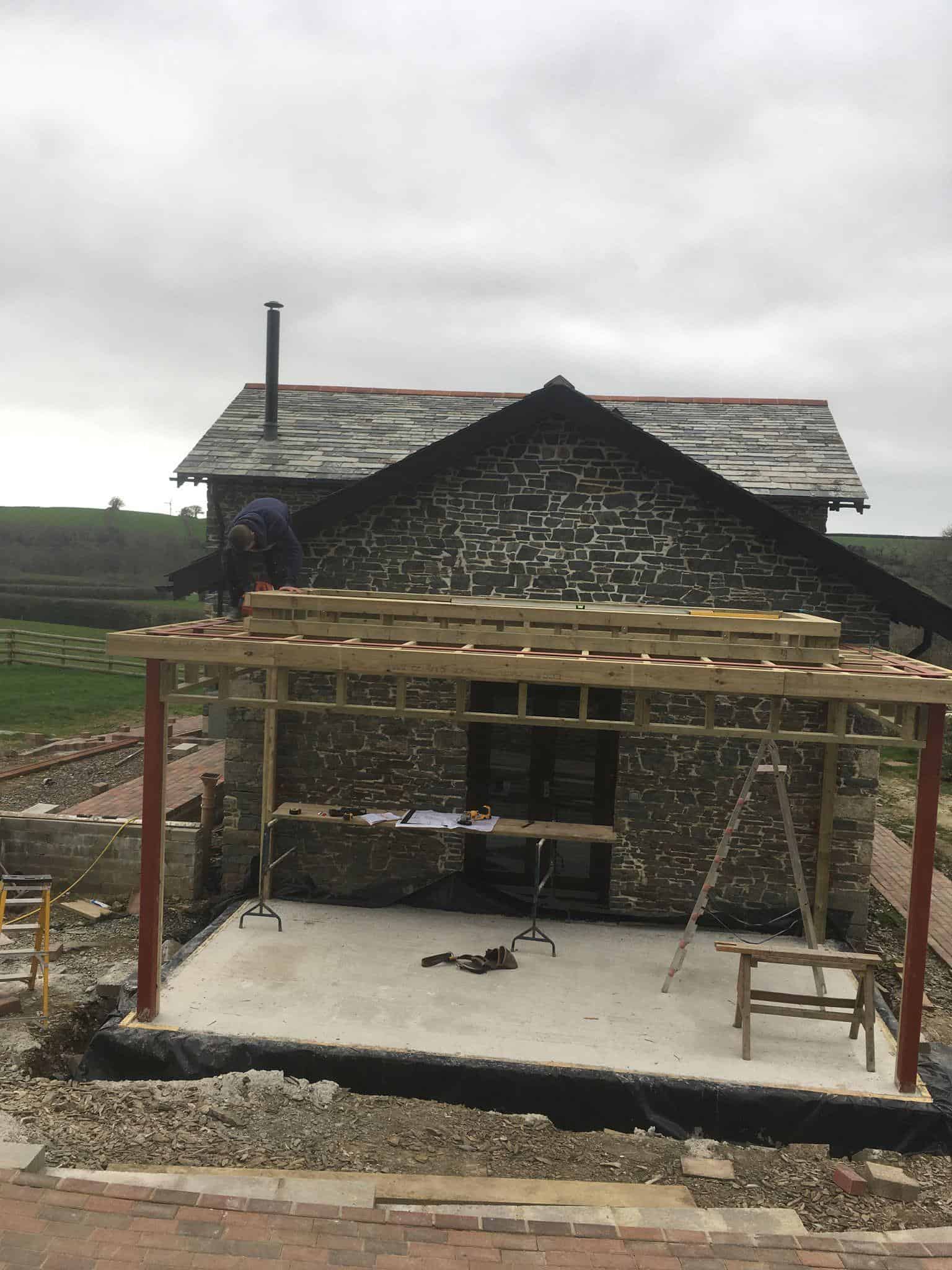 Newly constructed patio deck with wooden frame, stone house background, outdoor building project at JB Carpentry & Construction.