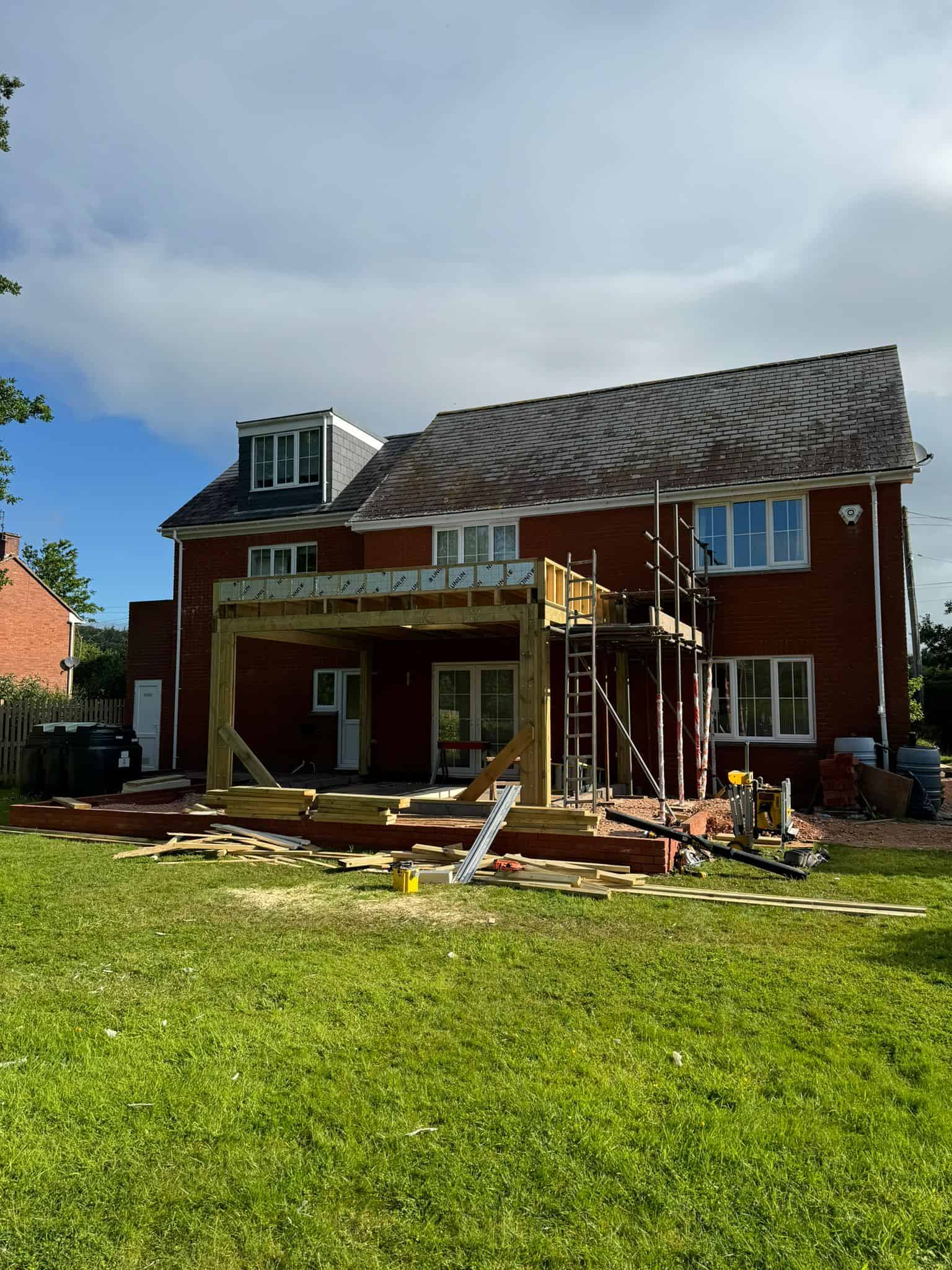 New patio construction in progress at a red brick house, featuring timber framework and scaffolding for renovation work.
