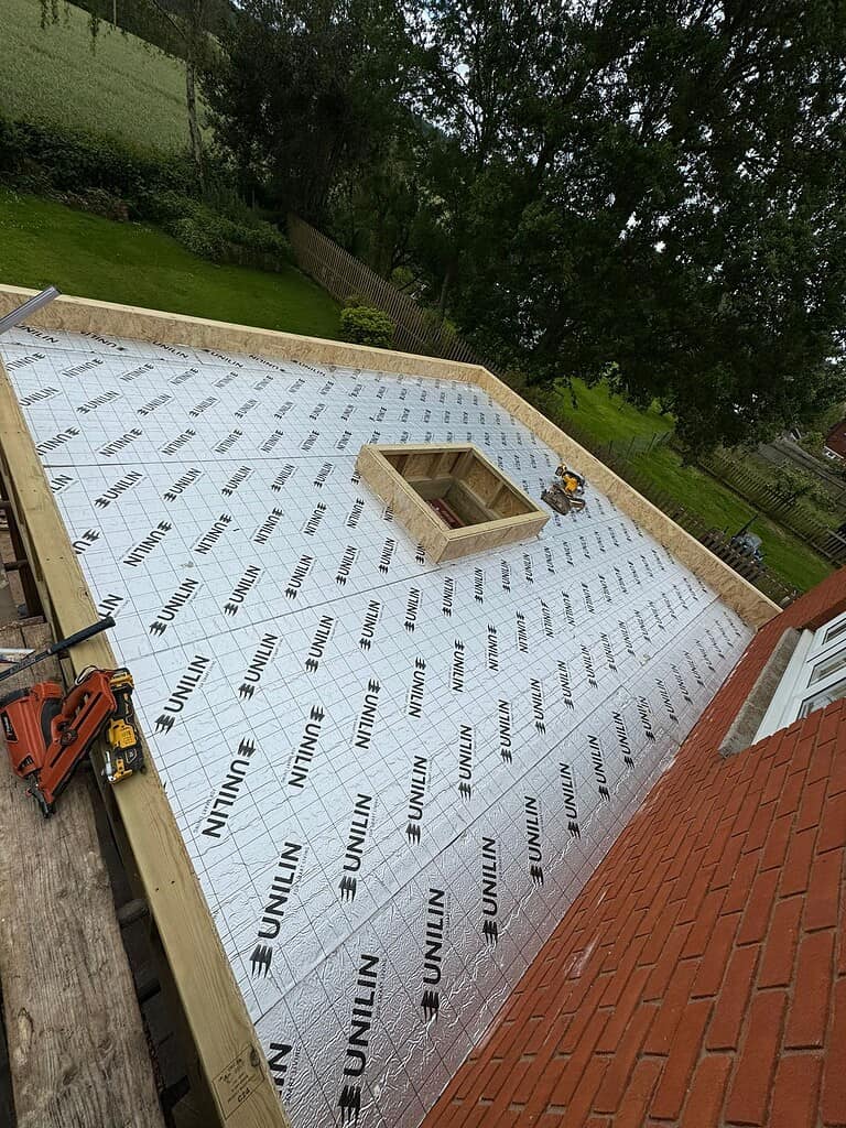 Insulated flat roof under construction with waterproofing membrane in progress.