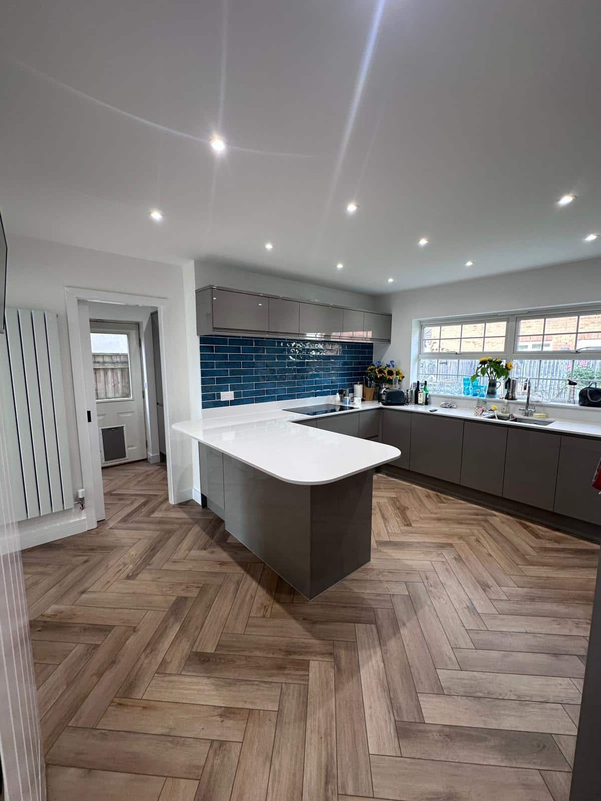 Modern grey kitchen with island, blue tiled backsplash, and wooden herringbone flooring for stylish home renovation.