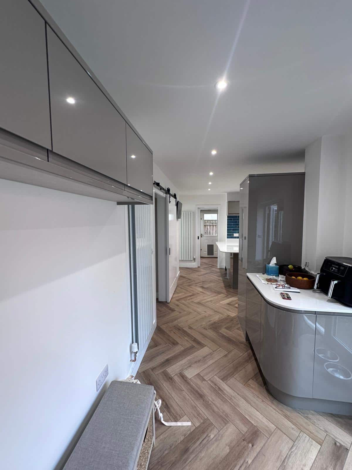 Bright modern kitchen with grey cabinetry and wooden herringbone flooring, showcasing expert carpentry and construction work.