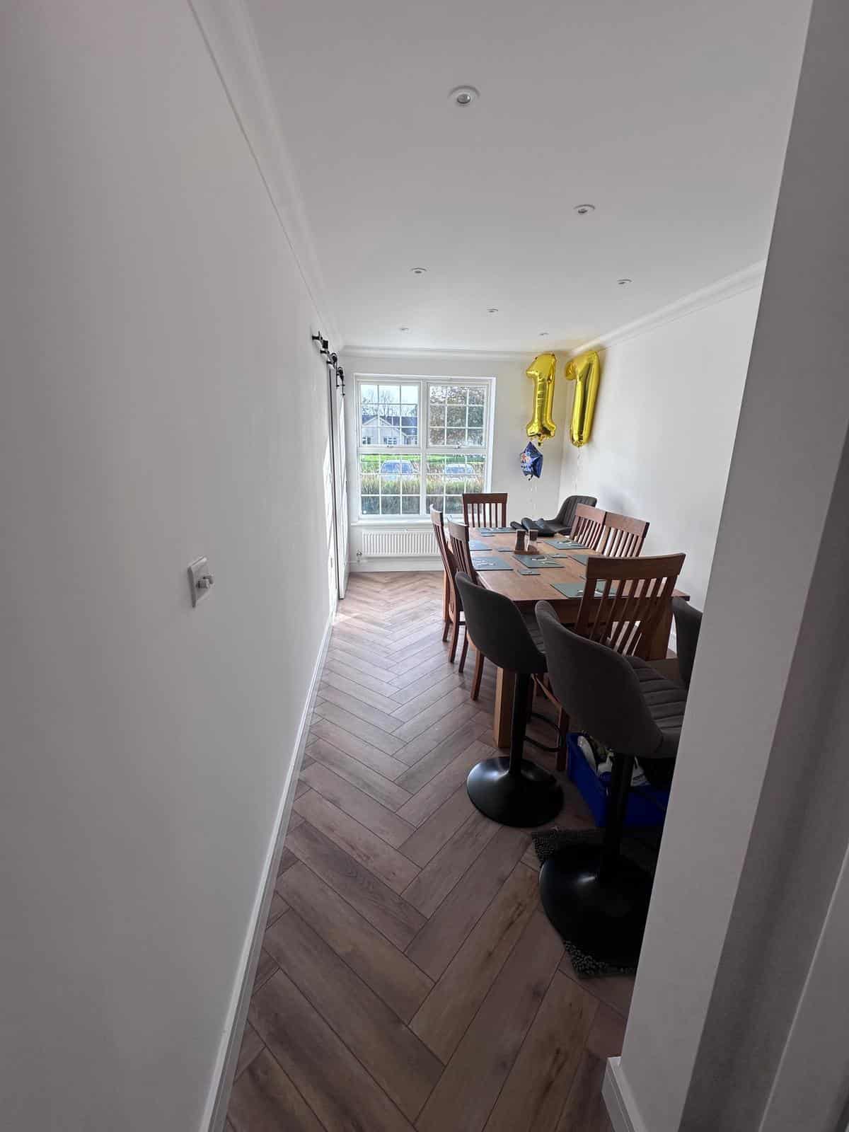 Bright modern dining room with wooden flooring and white walls, featuring birthday balloons on the wall.