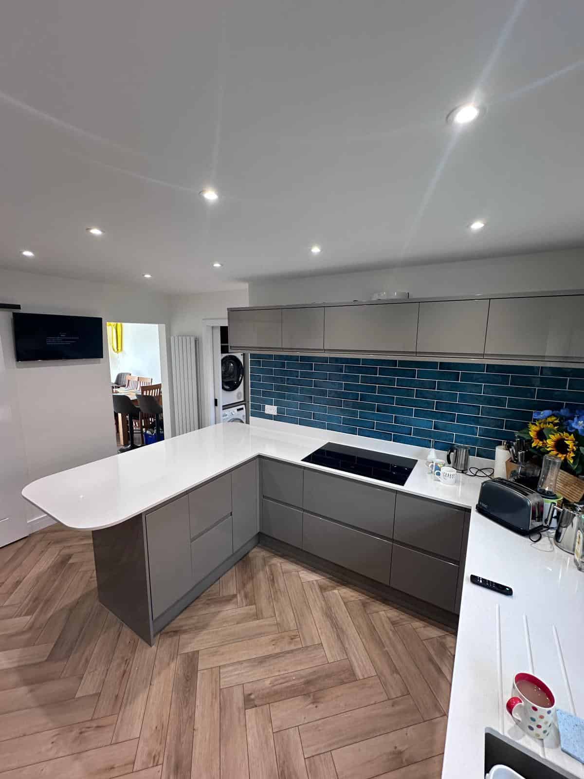 Modern kitchen with grey cabinets and white countertop, featuring custom carpentry and construction work.